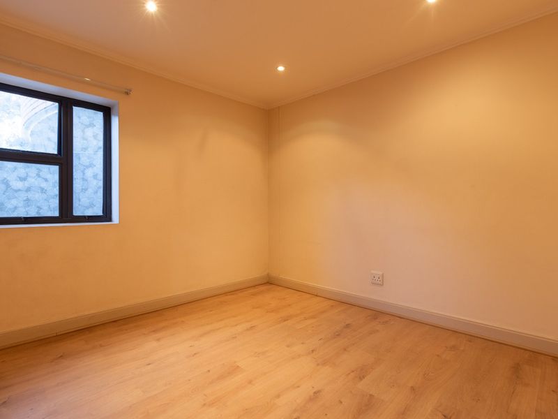 A bright, empty bedroom featuring light-toned laminate flooring, recessed ceiling lighting, and a modern aluminium-framed window.
