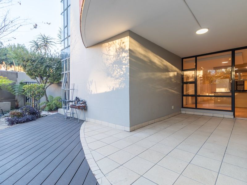 A spacious covered patio featuring a combination of composite decking and tiled flooring, seamlessly connecting to the interior living area through large glass doors.