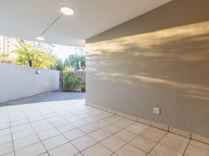 A covered outdoor patio area featuring tiled flooring, neutral wall finishes, and integrated lighting, providing a versatile space for outdoor relaxation.