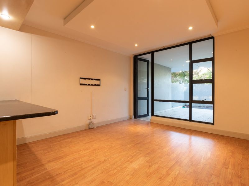 Open plan living area featuring laminate flooring, recessed ceiling lighting, and a large black-framed glass door providing access to an outdoor patio area.