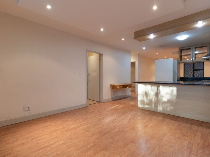 An open-plan living and kitchen area featuring modern laminate flooring, recessed lighting, and a functional kitchen island with stone countertops.