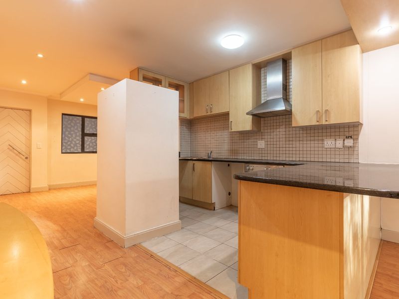 Open plan kitchen area featuring light wood cabinetry, granite countertops, and a stainless steel extractor fan, seamlessly flowing into the adjacent living space.