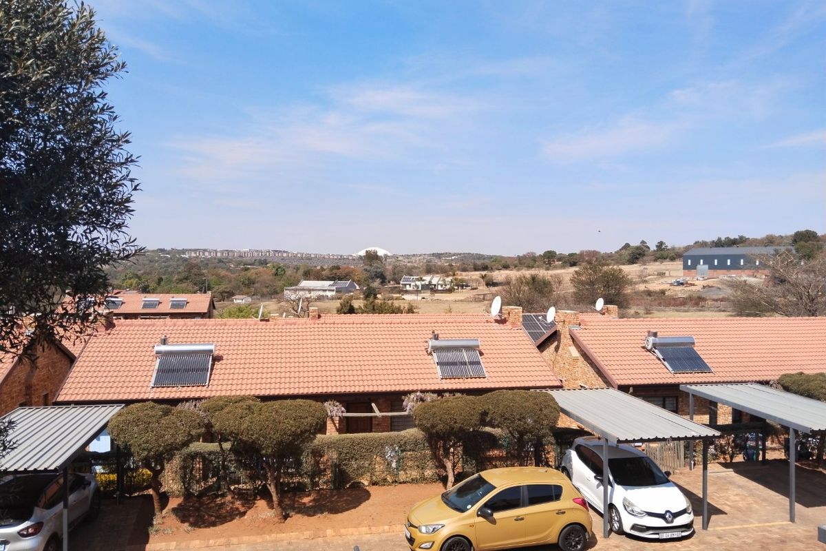 An elevated view of the rear exterior featuring a paved parking area with carports, tiled roofs with solar water heaters, and a scenic landscape view.