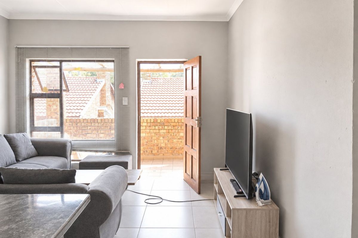 A bright living room featuring tiled flooring, neutral walls, and direct access to an outdoor balcony area through a timber door.
