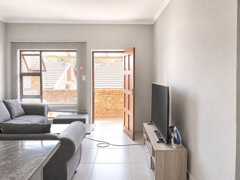 A bright living room featuring tiled flooring, neutral walls, and direct access to an outdoor balcony area through a timber door.