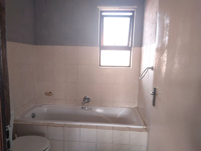 A functional bathroom featuring a built-in bathtub, tiled splashback, and a toilet, requiring cosmetic updates to improve its overall aesthetic appeal.