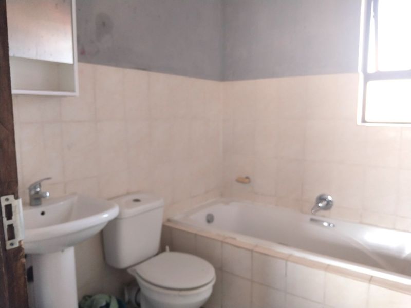 A functional bathroom featuring a pedestal basin, toilet, and bathtub with tiled walls, currently requiring cosmetic updates and finishing touches.