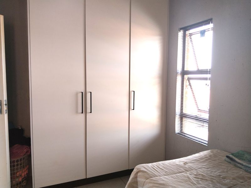 A bedroom featuring white built-in cupboards and a window with fitted venetian blinds, providing natural light and storage space.