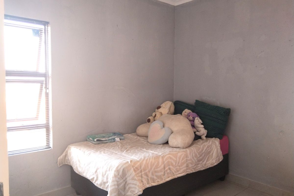 A simple bedroom featuring tiled flooring and a window with horizontal blinds, requiring minor cosmetic updates to the wall finishes.
