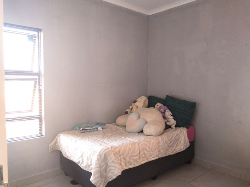 A simple bedroom featuring tiled flooring and a window with horizontal blinds, requiring minor cosmetic updates to the wall finishes.