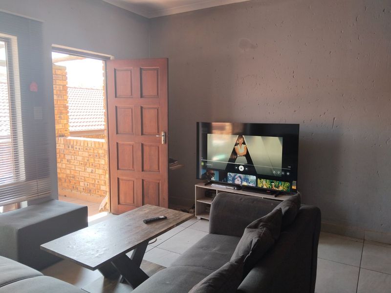 A living room area featuring tiled flooring, a timber door leading to a balcony, and venetian blinds.