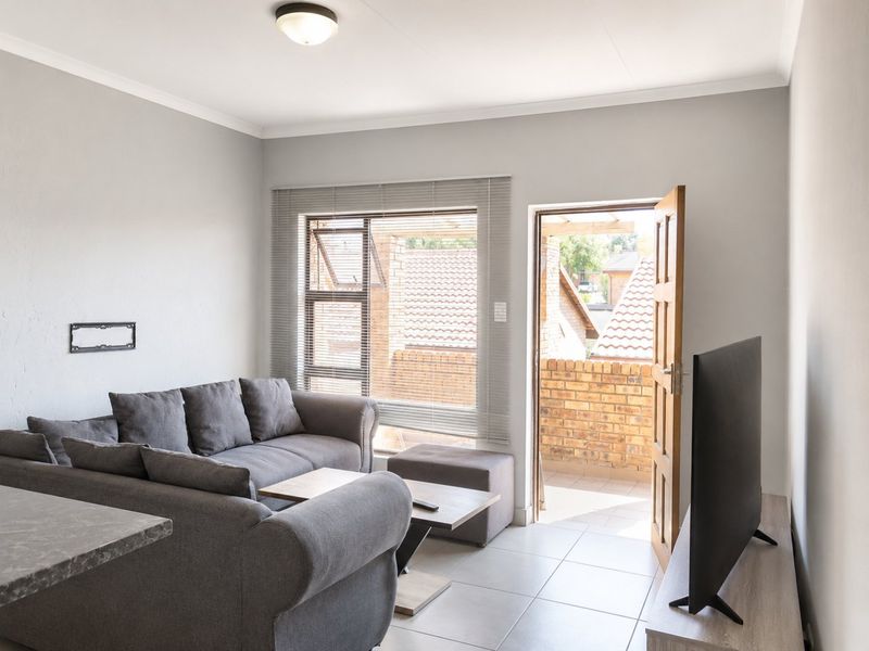 Open plan living area featuring tiled floors, neutral walls, and direct access to a private balcony through a timber door.
