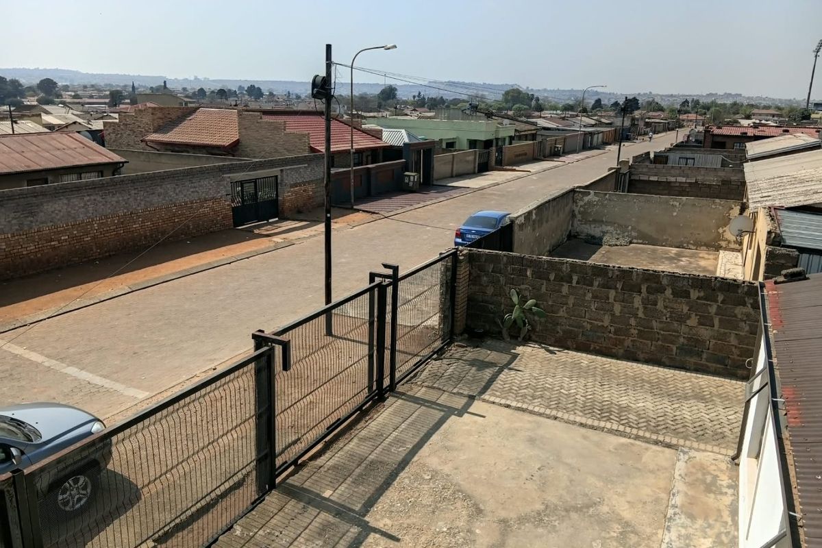 An elevated view of the property exterior showing the paved driveway, perimeter wall, and metal fencing overlooking the surrounding residential street.