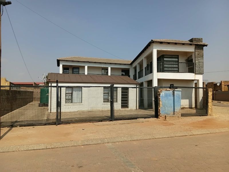 Front view of a two-story residential property featuring a metal security gate, perimeter fencing, and a balcony with stone cladding accents.
