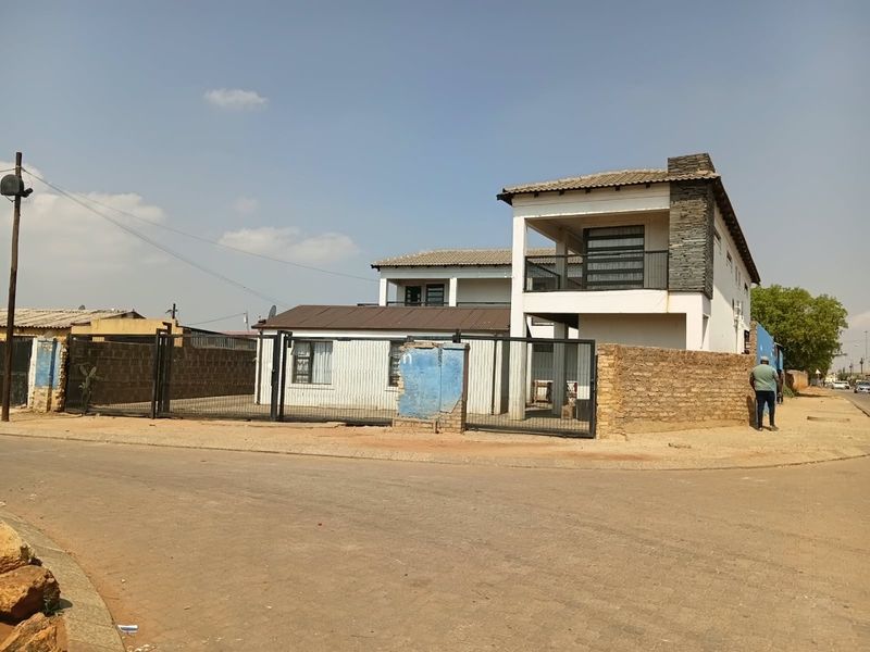 Street view of a two-story residential property featuring a metal security gate, stone cladding accents, and a balcony.