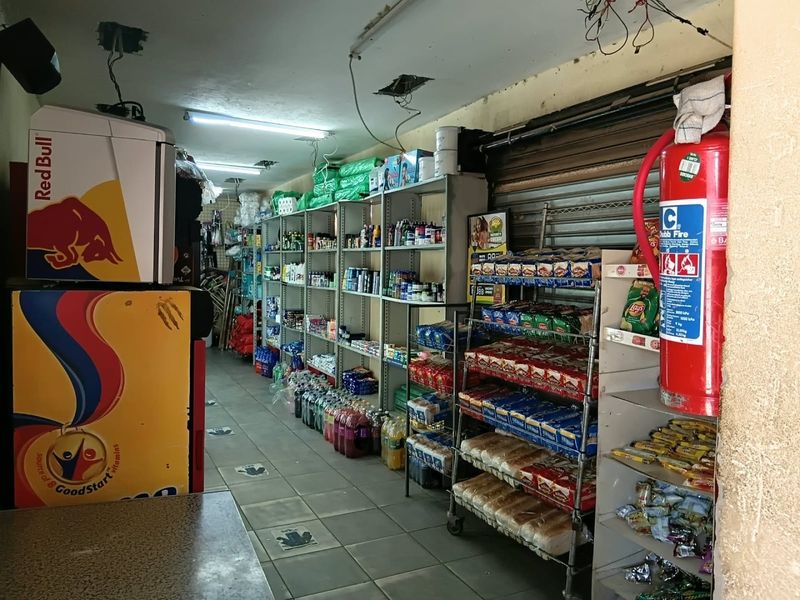 A commercial utility or retail storage space featuring tiled flooring, metal shelving units, and a roller shutter door with visible ceiling and electrical maintenance requirements.