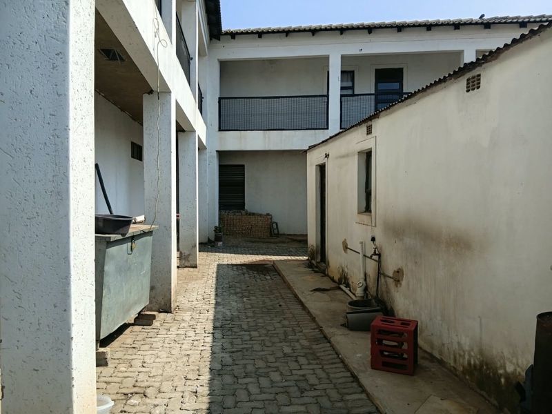 A rear courtyard area featuring paved flooring, covered balcony access, and exterior walls showing signs of wear and weathering.