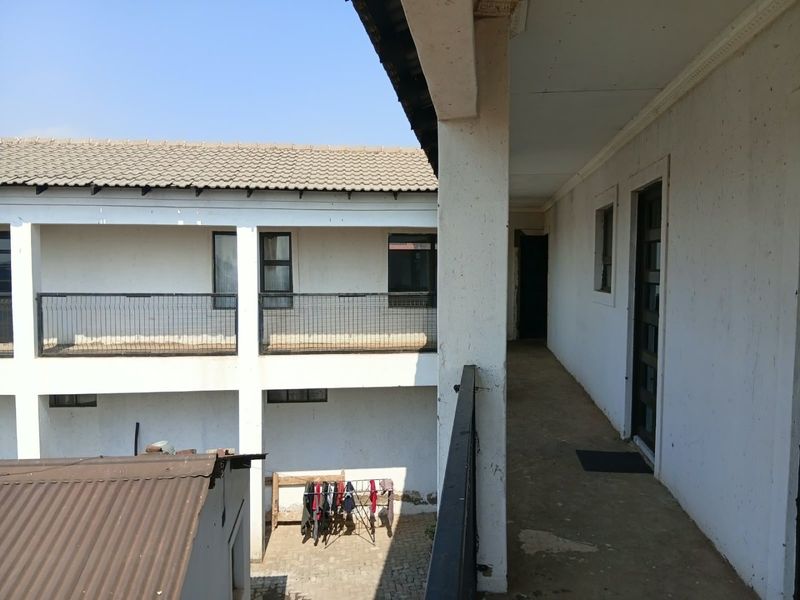 An exterior walkway balcony featuring metal railings and concrete flooring, showing signs of wear and requiring maintenance to the exterior wall finishes.