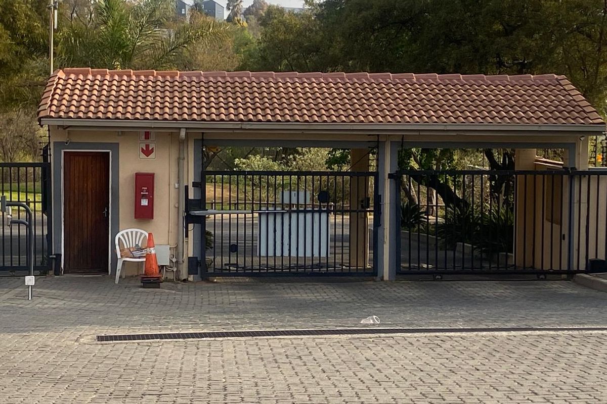 A secure gated entrance featuring a tiled roof guard house, metal security gates, and a paved driveway approach.