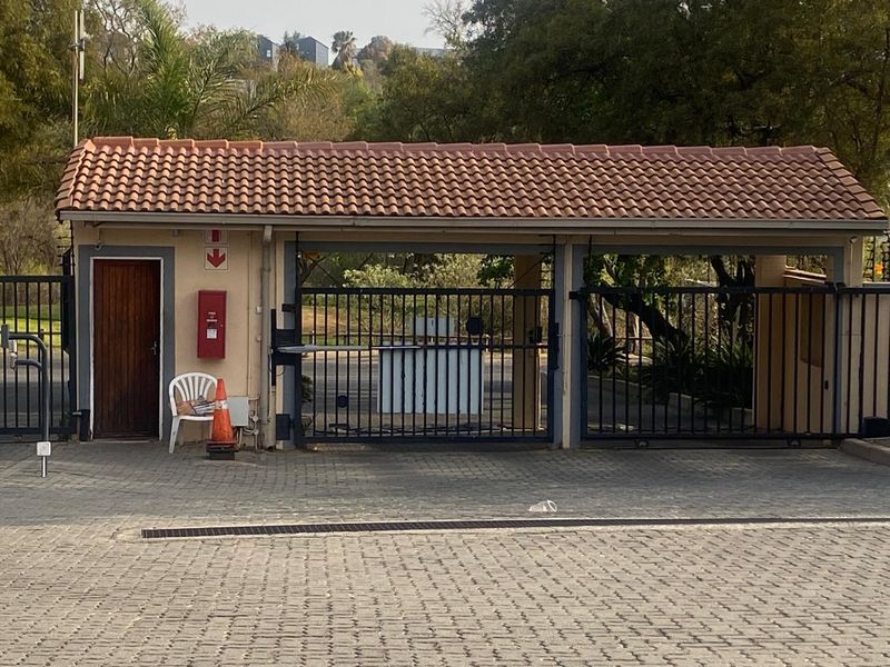 A secure gated entrance featuring a tiled roof guard house, metal security gates, and a paved driveway approach.