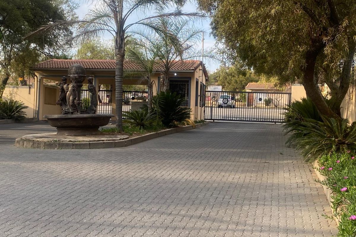 Front entrance view of the property featuring a paved driveway, security gate, guard house, and a decorative water fountain.