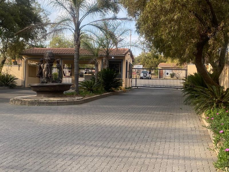 Front entrance view of the property featuring a paved driveway, security gate, guard house, and a decorative water fountain.