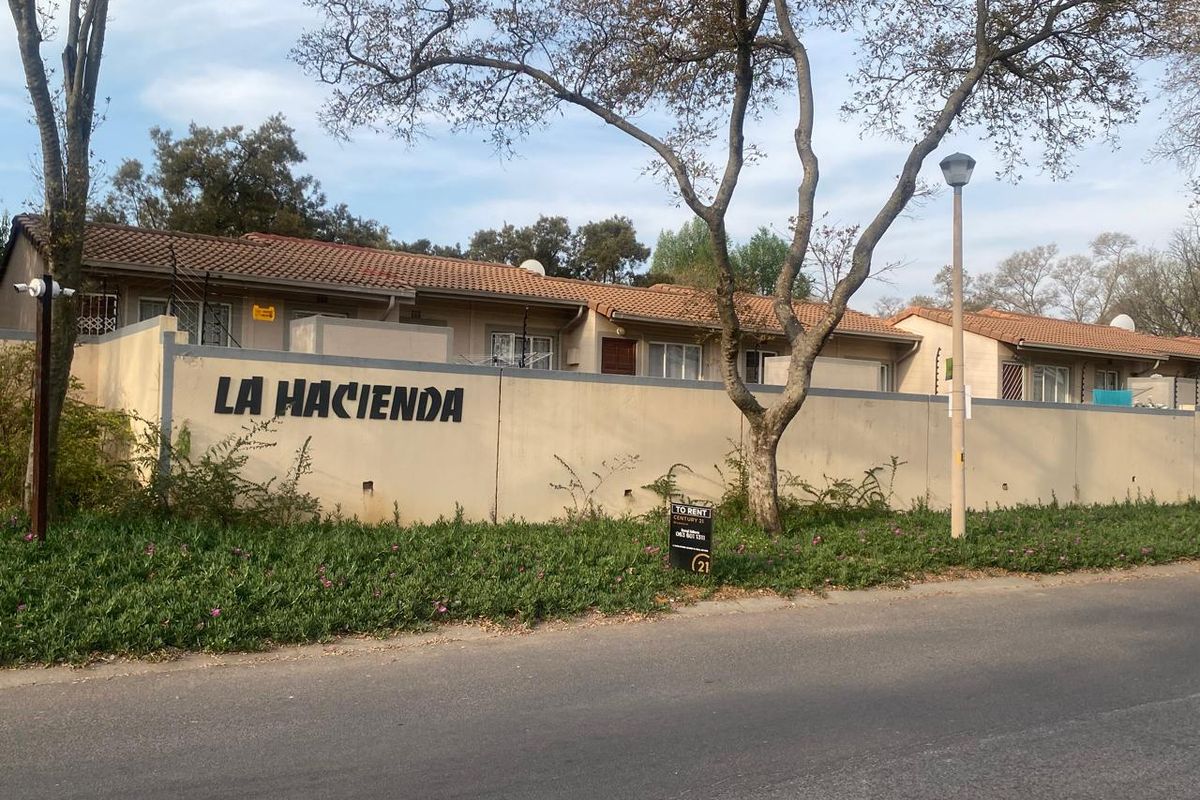 Street view of the La Hacienda complex, featuring a perimeter wall with electric fencing and tiled roof residential units.