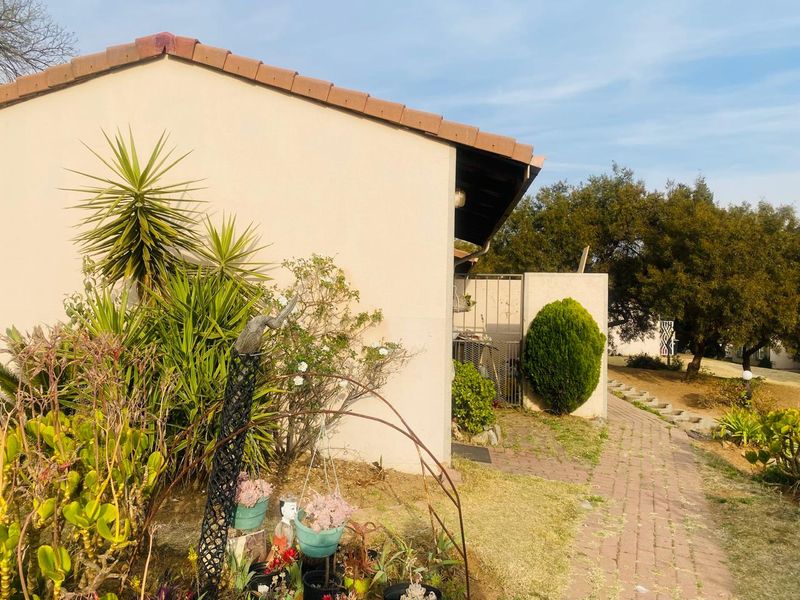 A view of the rear exterior of the house featuring a tiled roof, brick paved pathway, and established garden area.