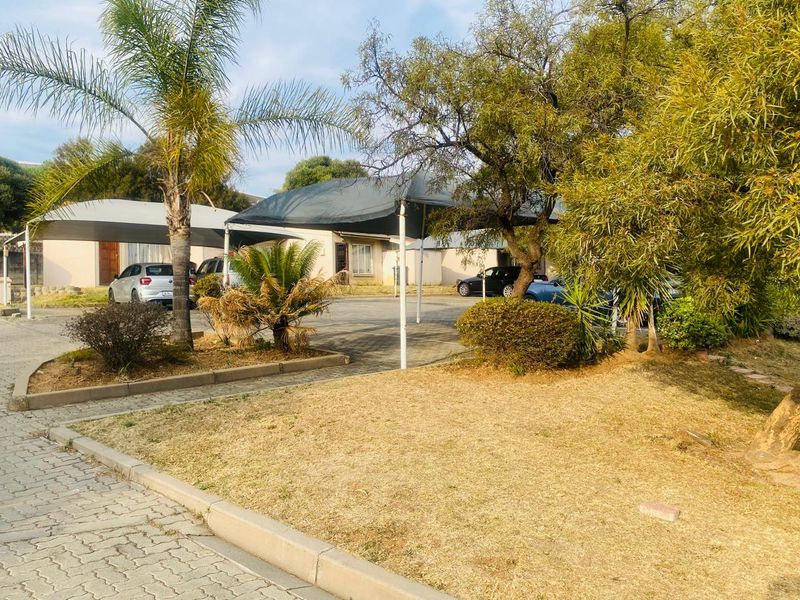 Front exterior view of the property featuring a paved driveway with shade cloth carports and established garden areas.