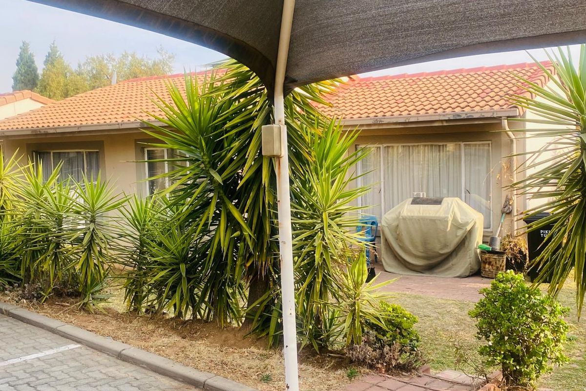 Rear exterior view of the house featuring a paved patio area, sliding glass doors, and a shade sail structure.