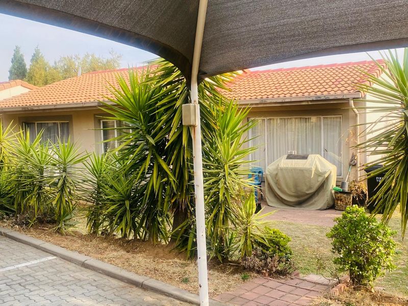 Rear exterior view of the house featuring a paved patio area, sliding glass doors, and a shade sail structure.