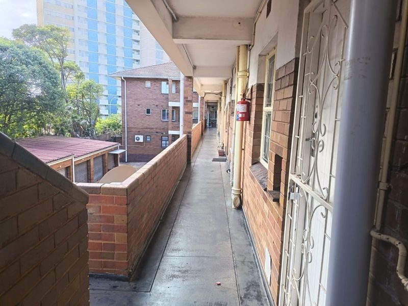 An exterior apartment building walkway featuring brick walls, a security gate, and a fire extinguisher, providing access to residential units.