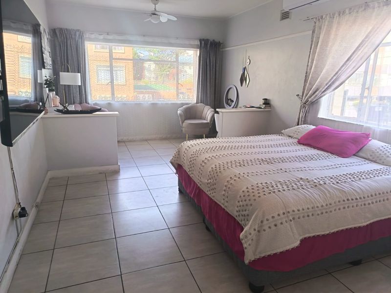 Spacious bedroom featuring tiled flooring, a ceiling fan, and a split-system air conditioner, with large windows providing ample natural light.