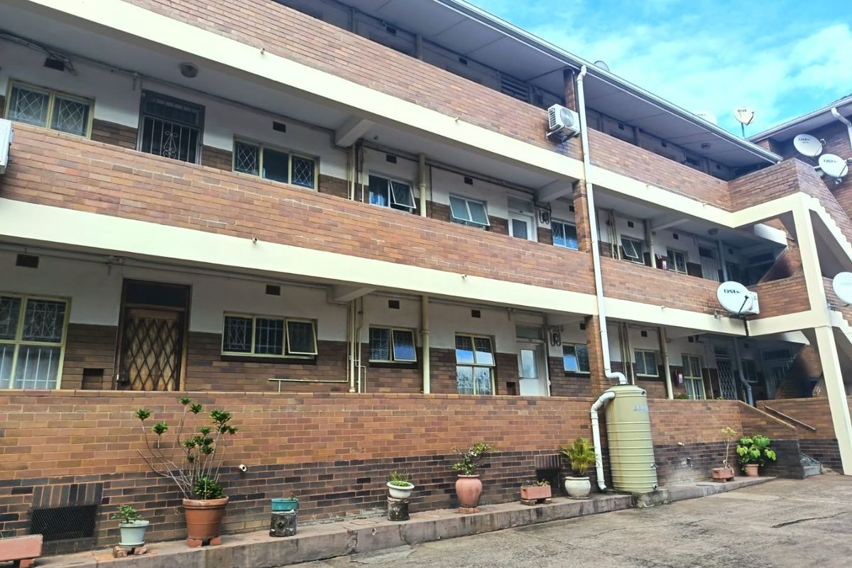 A multi-story apartment building exterior featuring face brick construction, security-fitted windows, and external water storage infrastructure.