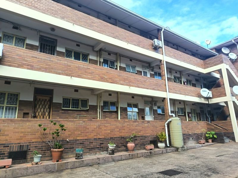 A multi-story apartment building exterior featuring face brick construction, security-fitted windows, and external water storage infrastructure.