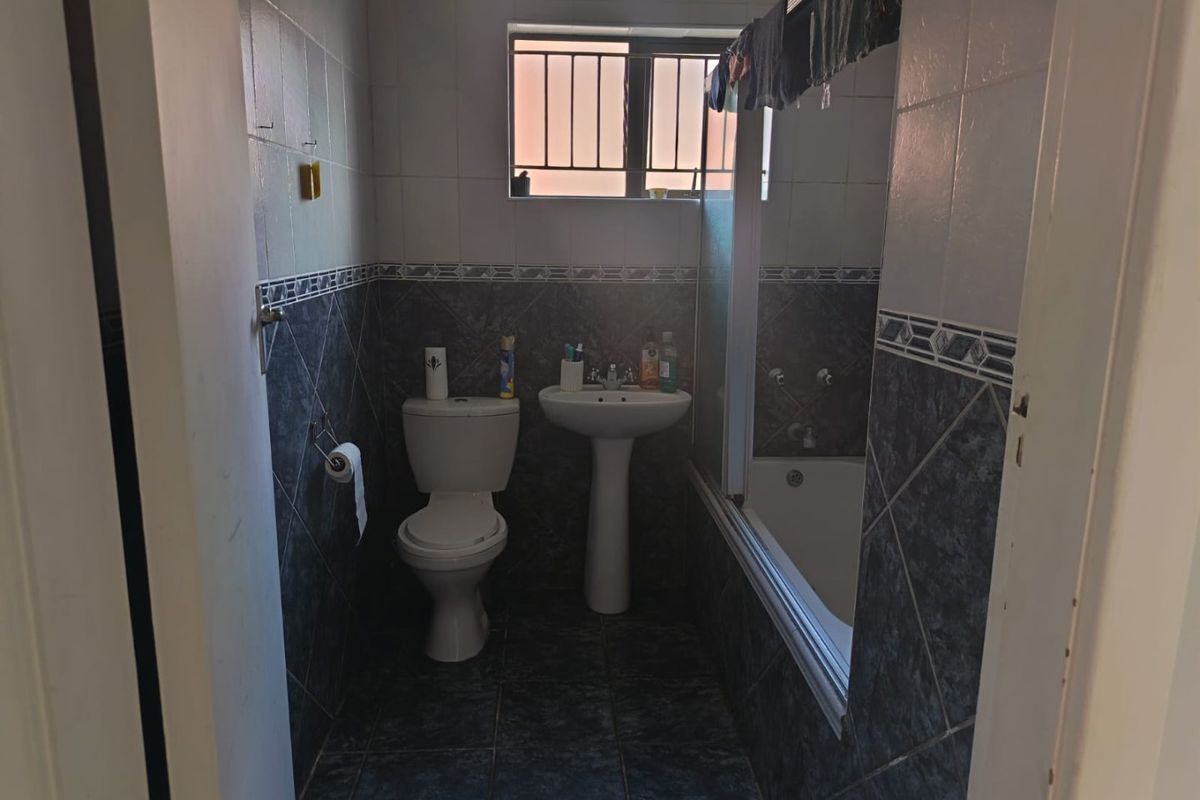 A functional bathroom featuring a pedestal basin, toilet, and a bathtub with a shower screen, finished with tiled walls and flooring.