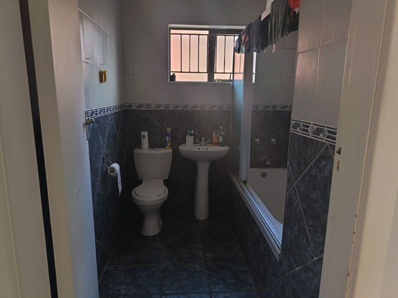 A functional bathroom featuring a pedestal basin, toilet, and a bathtub with a shower screen, finished with tiled walls and flooring.
