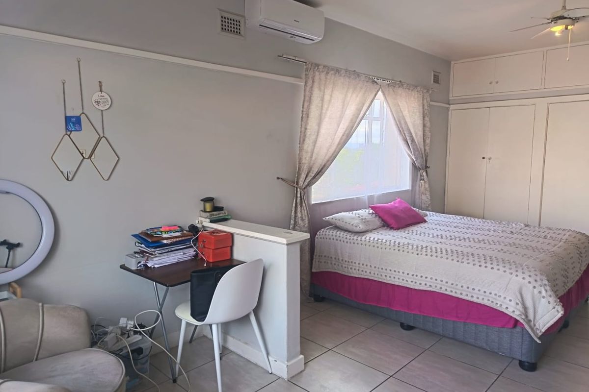 A bedroom featuring built-in cupboards, tiled flooring, a ceiling fan, and an air conditioning unit, with a partial partition wall creating a workspace area.