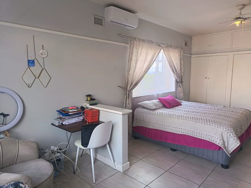 A bedroom featuring built-in cupboards, tiled flooring, a ceiling fan, and an air conditioning unit, with a partial partition wall creating a workspace area.