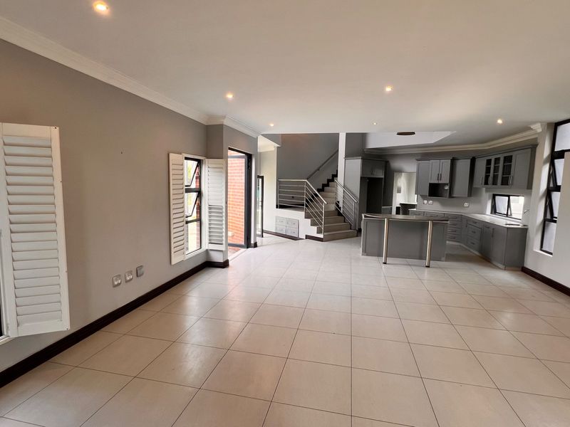 Spacious open-plan living and kitchen area featuring neutral tiled flooring, modern grey cabinetry, and a staircase with a contemporary metal balustrade.