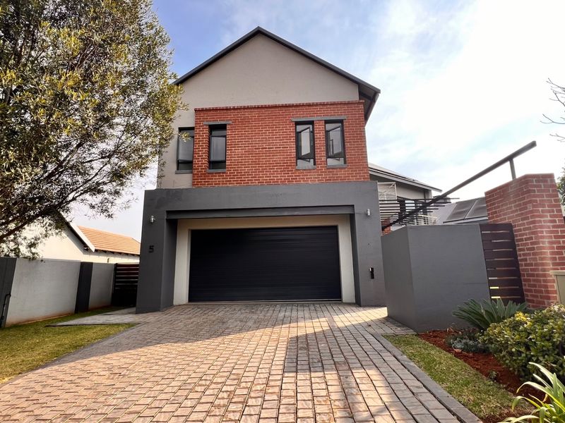 Modern double-story residential facade featuring a paved driveway, integrated double garage, and a combination of brick and rendered wall finishes.