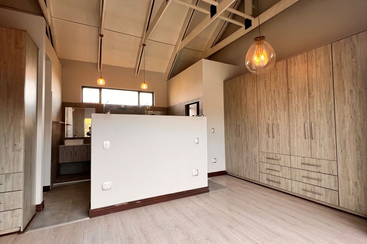 Spacious bedroom featuring high vaulted ceilings with exposed rafters, extensive built-in cabinetry, laminate flooring, and an integrated en-suite bathroom area.