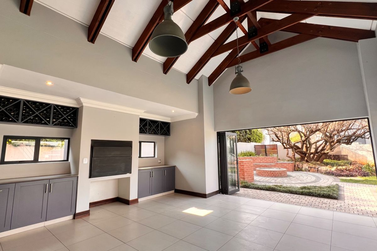 Spacious living area featuring exposed timber trusses, built-in cabinetry with wine storage, a fireplace, and seamless access to the outdoor patio through stacking doors.