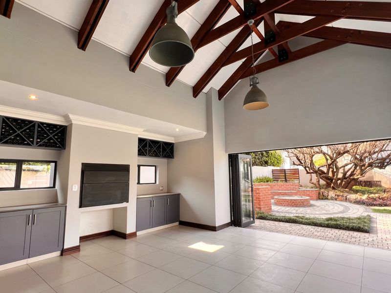 Spacious living area featuring exposed timber trusses, built-in cabinetry with wine storage, a fireplace, and seamless access to the outdoor patio through stacking doors.