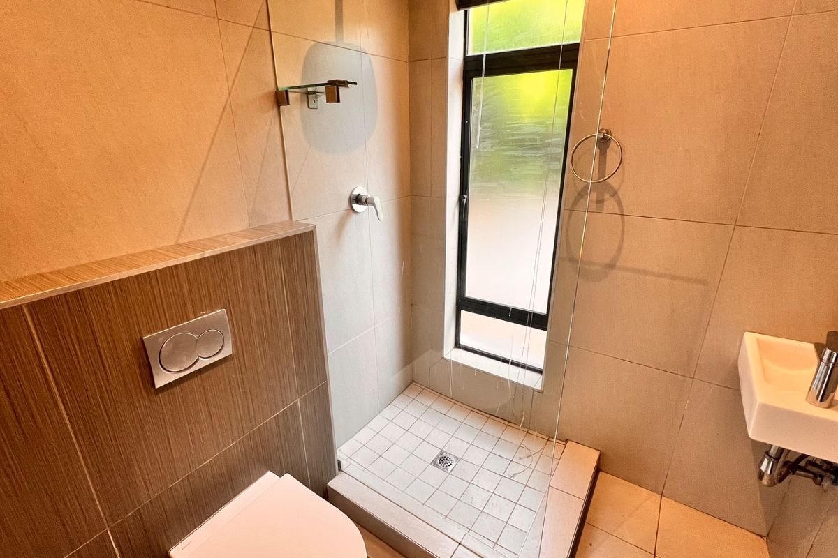 Modern bathroom featuring a wall-mounted toilet with dual flush, a walk-in shower with glass screen, and a wall-mounted basin with neutral tiling.