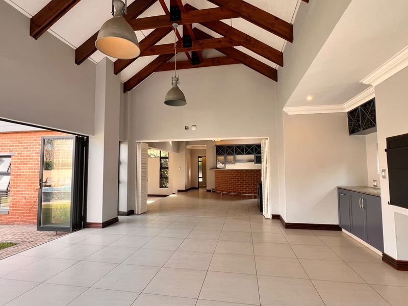 Spacious open-plan living area featuring vaulted ceilings with exposed timber trusses, tiled flooring, and a built-in bar, opening onto an outdoor patio area.