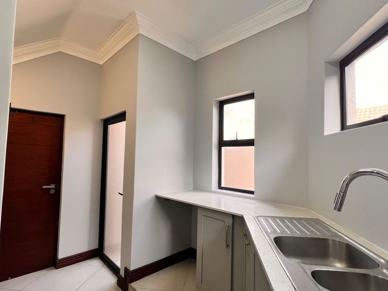 A clean and modern scullery featuring stone countertops, a double bowl sink with a gooseneck mixer, and ample built-in cabinetry.