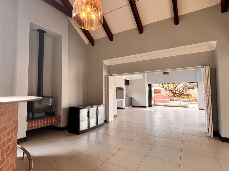 Spacious open-plan living area featuring vaulted ceilings with exposed beams, a brick bar, a fireplace, and seamless access to the outdoor patio.