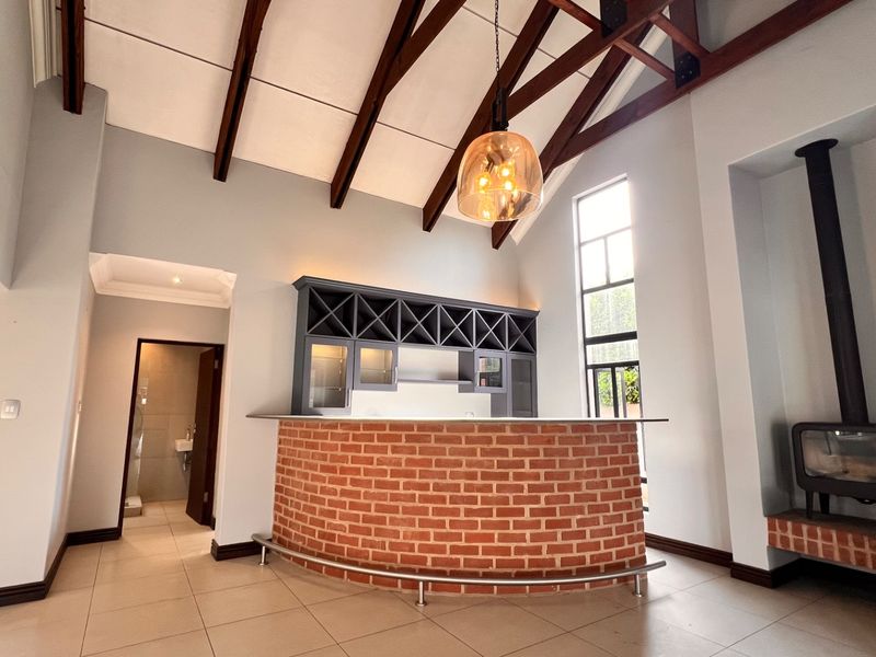 Spacious bar area featuring exposed timber rafters, a built-in brick counter with wine storage, and a modern wood-burning fireplace.