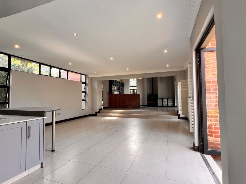 Spacious open-plan living area featuring a modern kitchen with gas hob, tiled flooring, recessed lighting, and a raised section with a brick fireplace.
